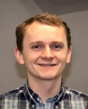Smiling man wearing plaid shirt, with a neutral background About Share The Harvest