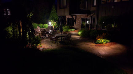 Backyard patio illuminated at night with landscape lighting