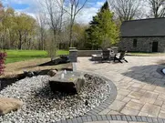 Paved patio with rock water feature, seating, and stone building