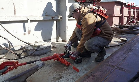 Worker securing equipment on a ship with tools and safety harness