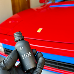 Gloved hand holding ZR53 bottle, red car being prepped