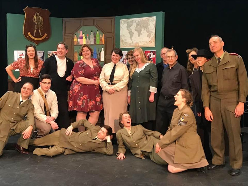 Group photo of actors on stage, wearing various costumes, smiling, and laughing. What's On Stage