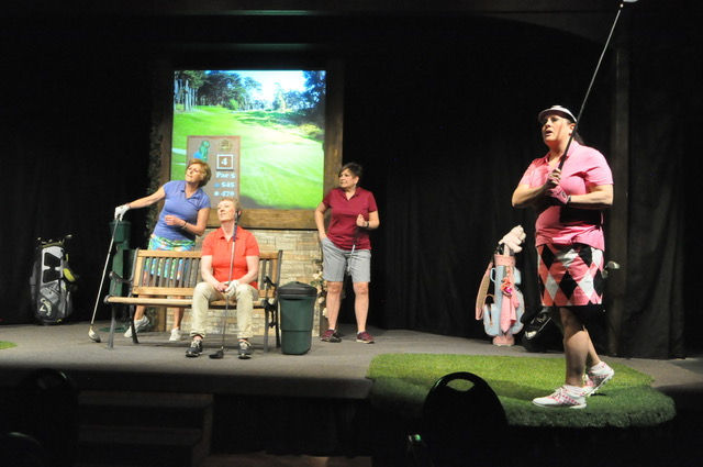 Women on stage with golf clubs and screen. What's on stage?