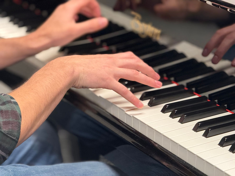 Hands playing a black and white piano keyboard, close-up. A person wears a plaid shirt. The mood is focused, showcasing a musical moment.