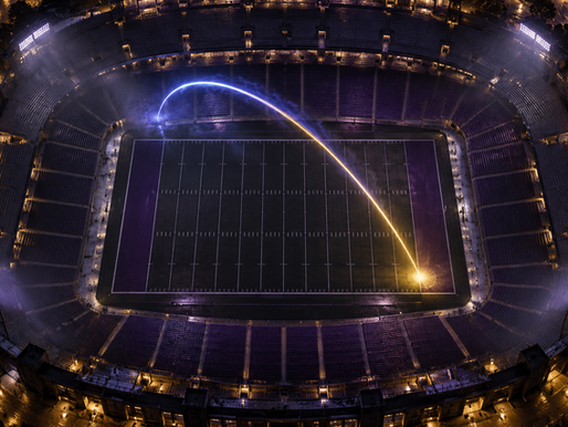 Aerial night stadium with a blue-and-gold trajectory arc landing near the corner inside the 10-yard line