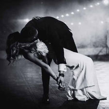 Groom dramatically dipping the bride on the dance floor for a passionate kiss during their first dance, with fog and string lights in the background adding to the cinematic atmosphere