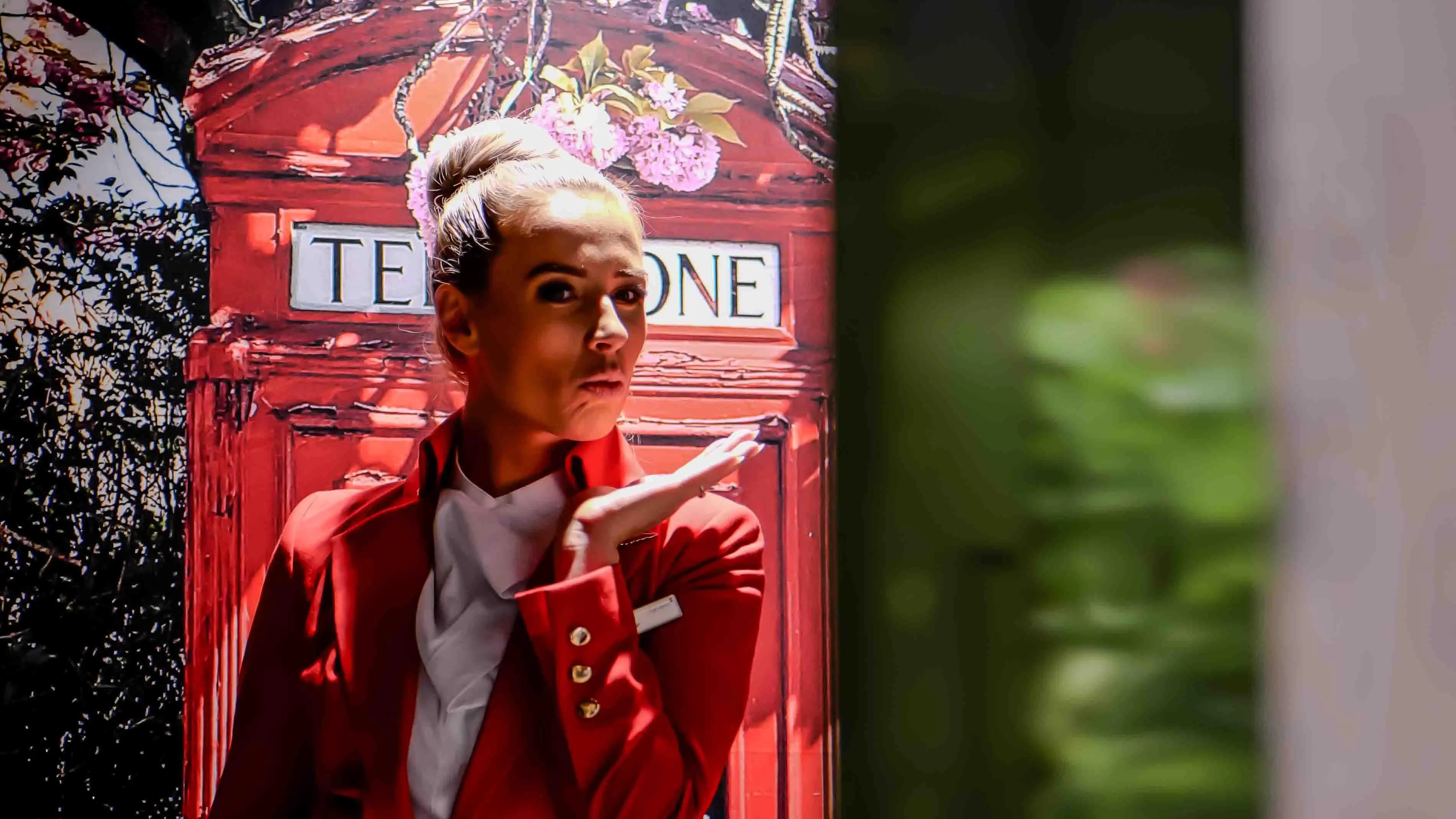 Virgin Atlantic flight attendant playfully posing in front of a classic red British telephone booth backdrop during the airline’s 30-year celebration event in San Francisco.