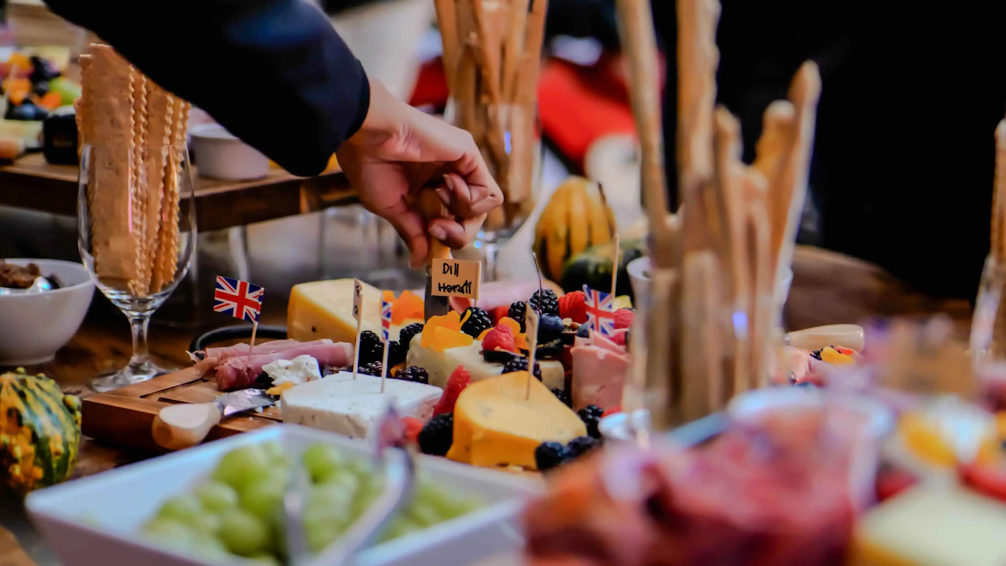 Close-up of a gourmet cheese and charcuterie platter with British flags, served at the Virgin Atlantic and British Consulate event in San Francisco, featuring dill havarti and fresh fruit.