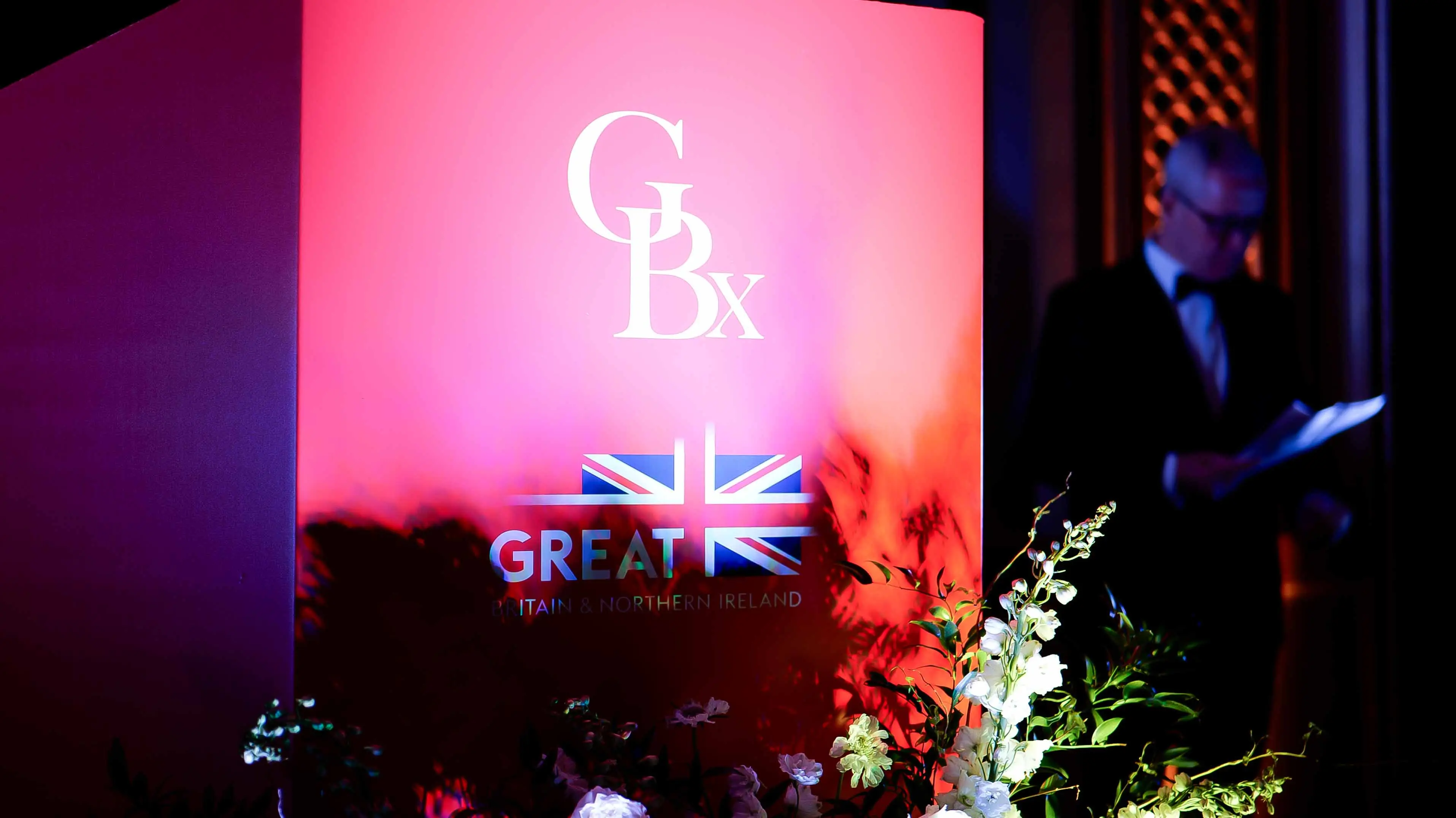 Illuminated GBx and GREAT Britain & Northern Ireland branding display at the GREAT GBx Gala 2024 in San Francisco, surrounded by floral arrangements and stage lighting.