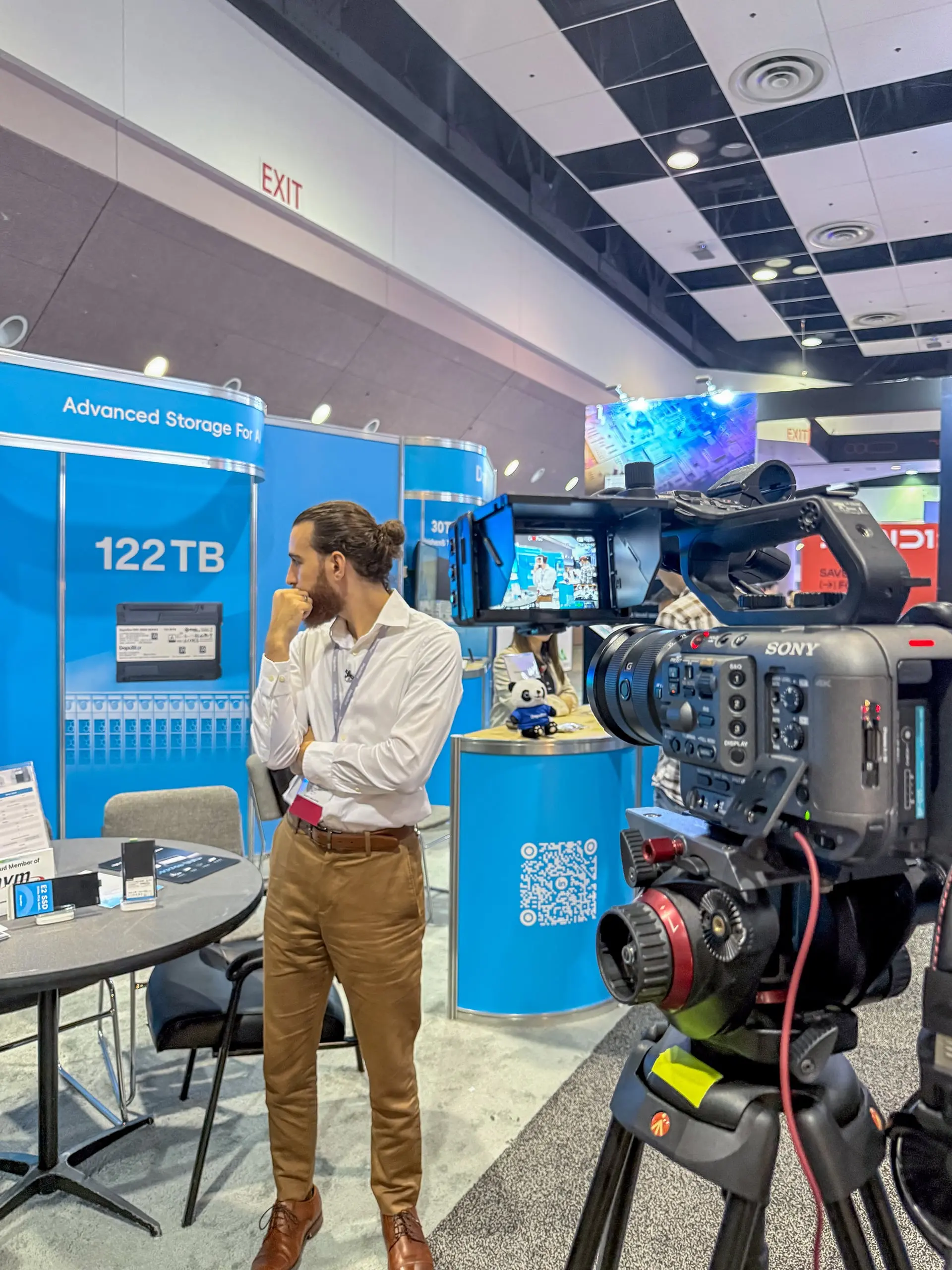 Sony FX3 camera with a 70-200mm f/2.8 lens mounted on a tripod recording a Dapustor representative at FMS 2025 booth in Santa Clara Convention Center, filmed by Saboor Bidar for corporate trade show videography.