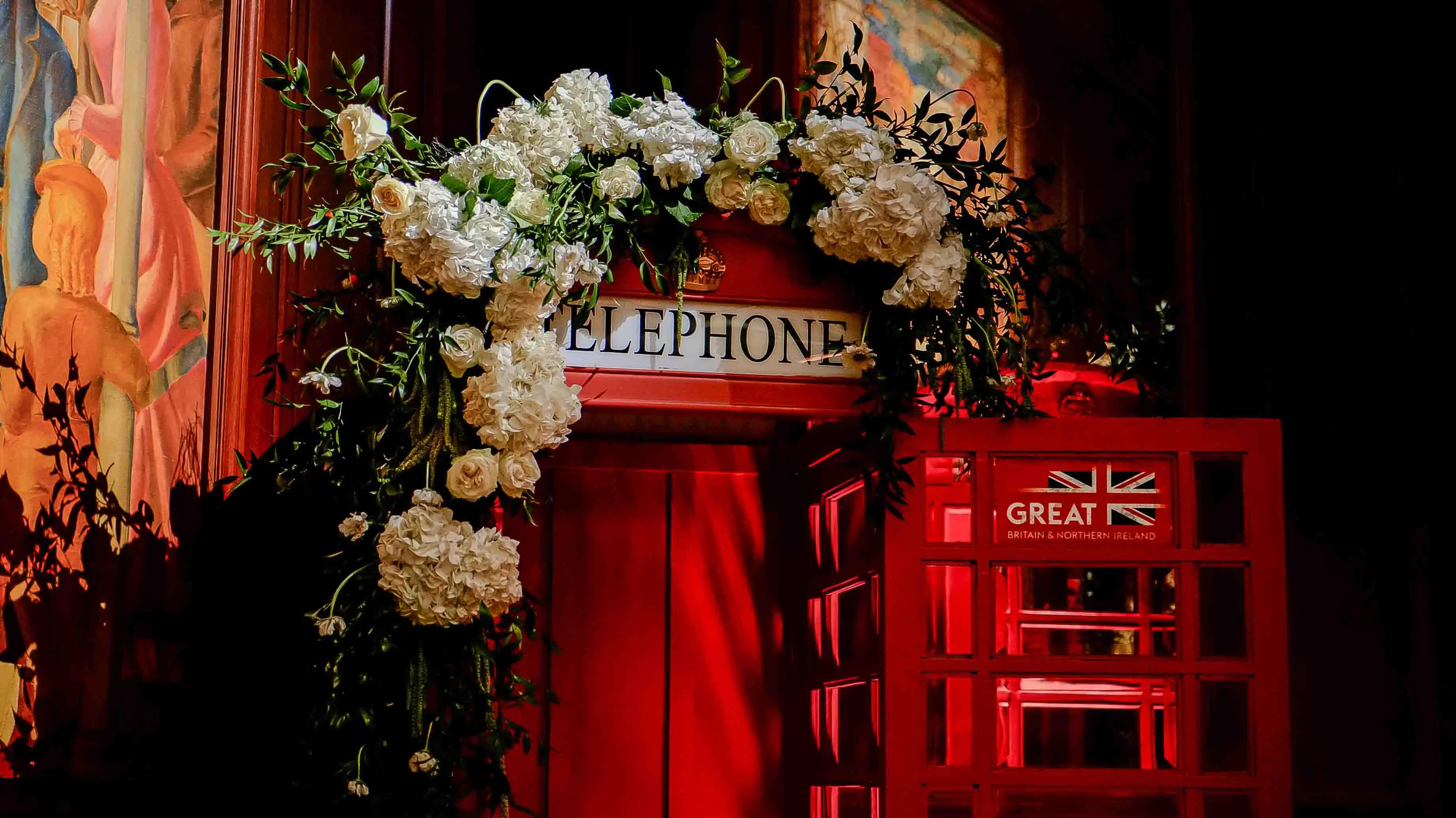 Decorated British red telephone booth adorned with white roses and floral arch, featuring the GREAT Britain & Northern Ireland logo at the GBx Gala 2024 in San Francisco.