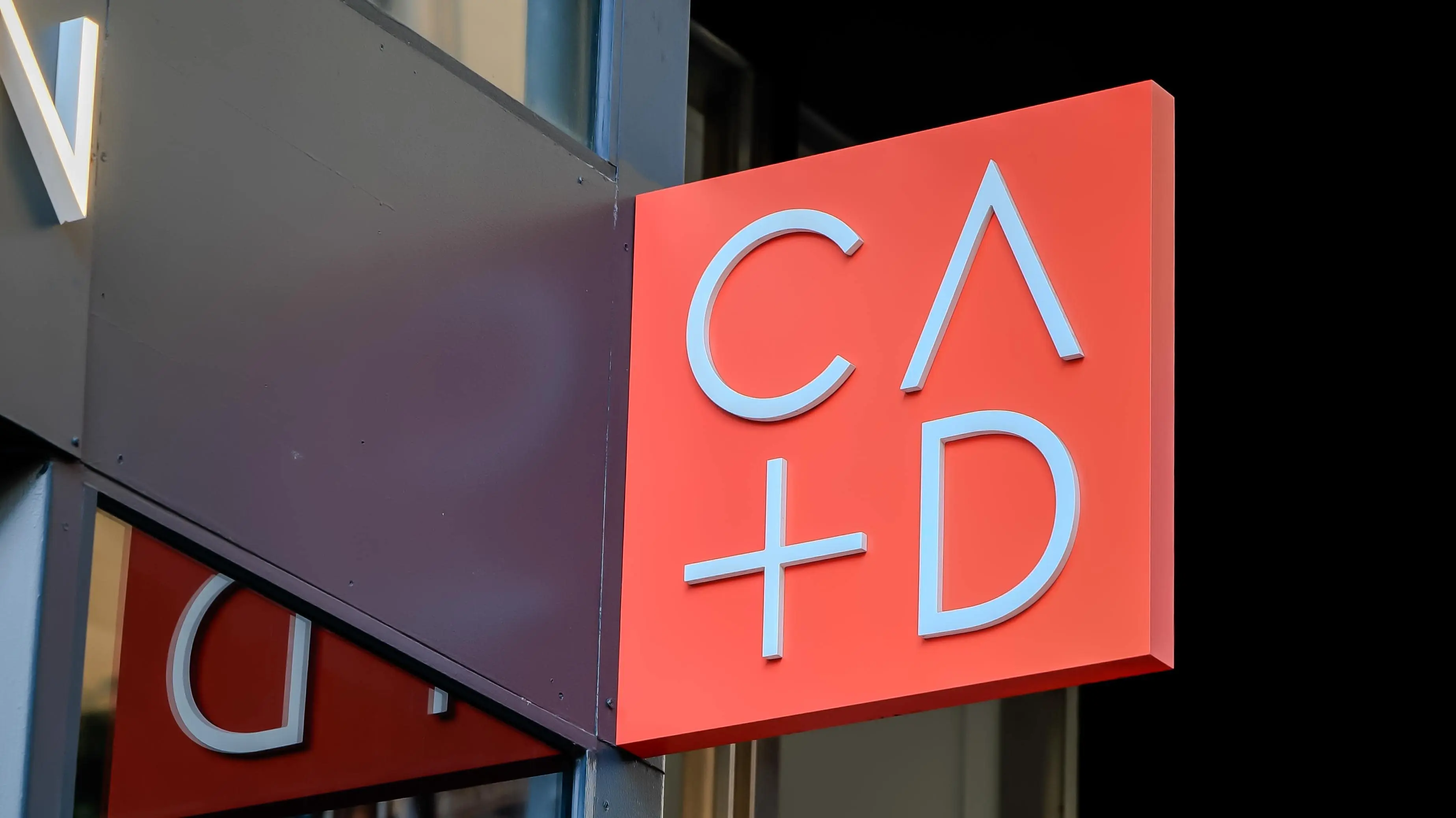 Red logo sign for the Center for Architecture + Design (CA+D) mounted outside the San Francisco venue entrance.