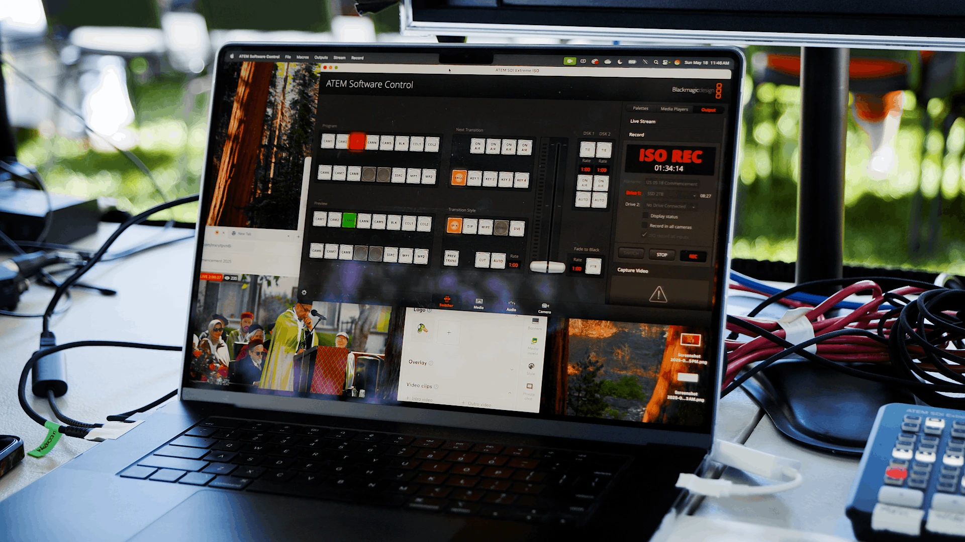 Laptop displaying a multi-camera live switching controller app with several video inputs and preview windows during an outdoor commencement live stream.
