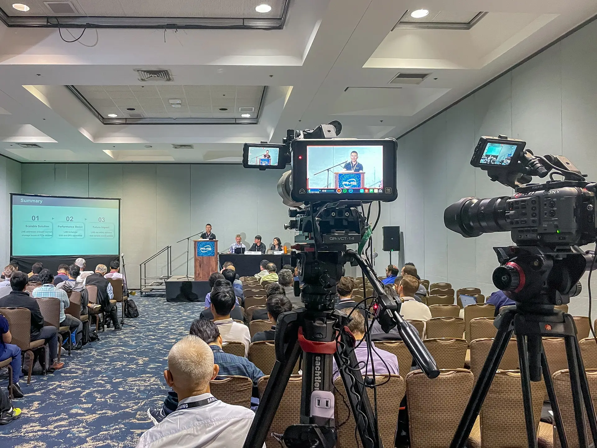 Multi-camera setup recording a panel discussion at FMS 2025 conference, Santa Clara Convention Center, with speakers and audience in session.