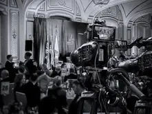 Professional video cameras recording the stage during the GREAT GBx Gala 2024 at the Palace Hotel in San Francisco, with a view of the audience and event branding in a grand ballroom setting. Filmed by Bidar Video