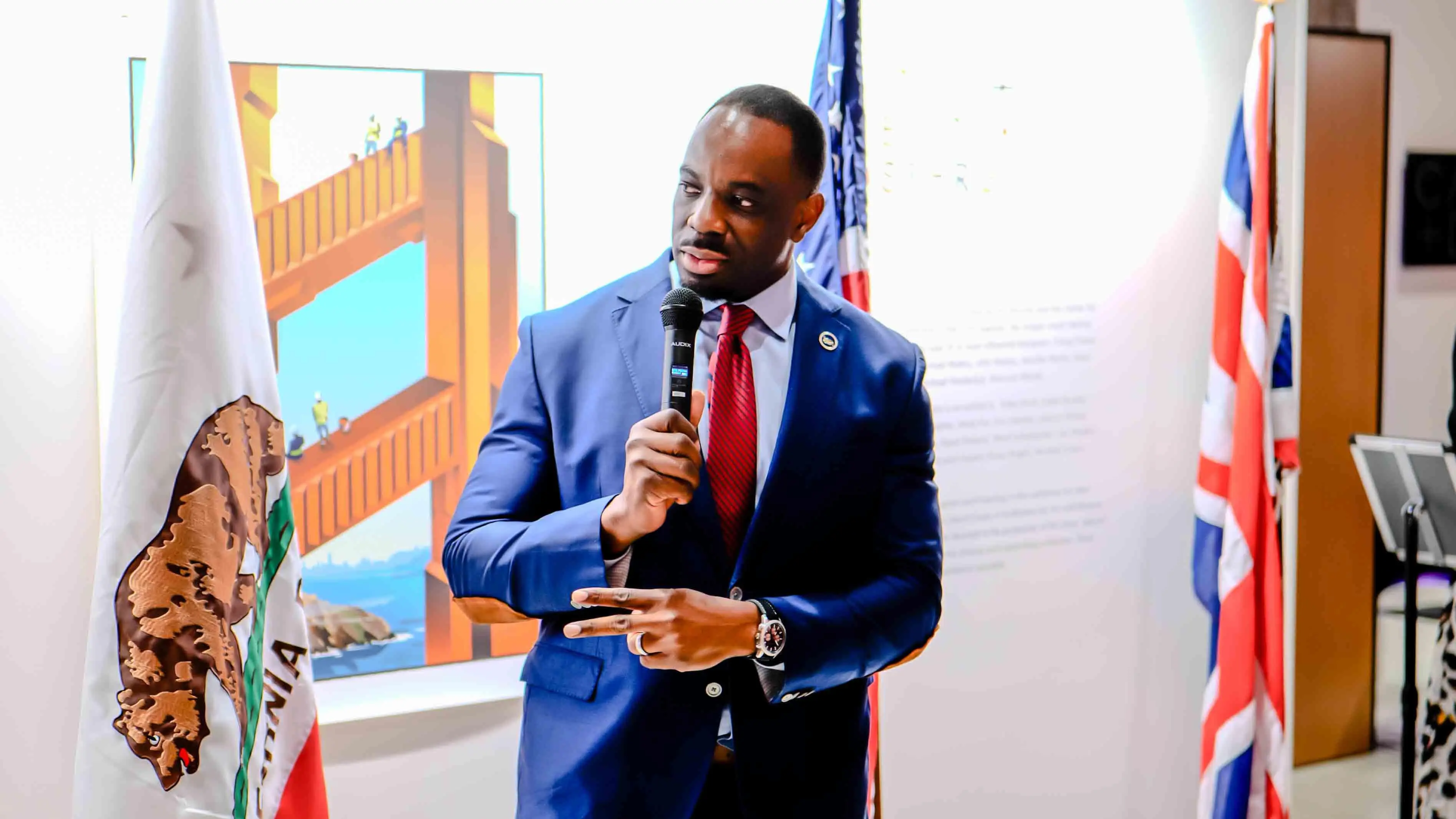 Guest speaker delivering remarks during the Virgin Atlantic and British Consulate 30-year celebration event in San Francisco, standing between the California, U.S., and UK flags at the Center for Architecture + Design.
