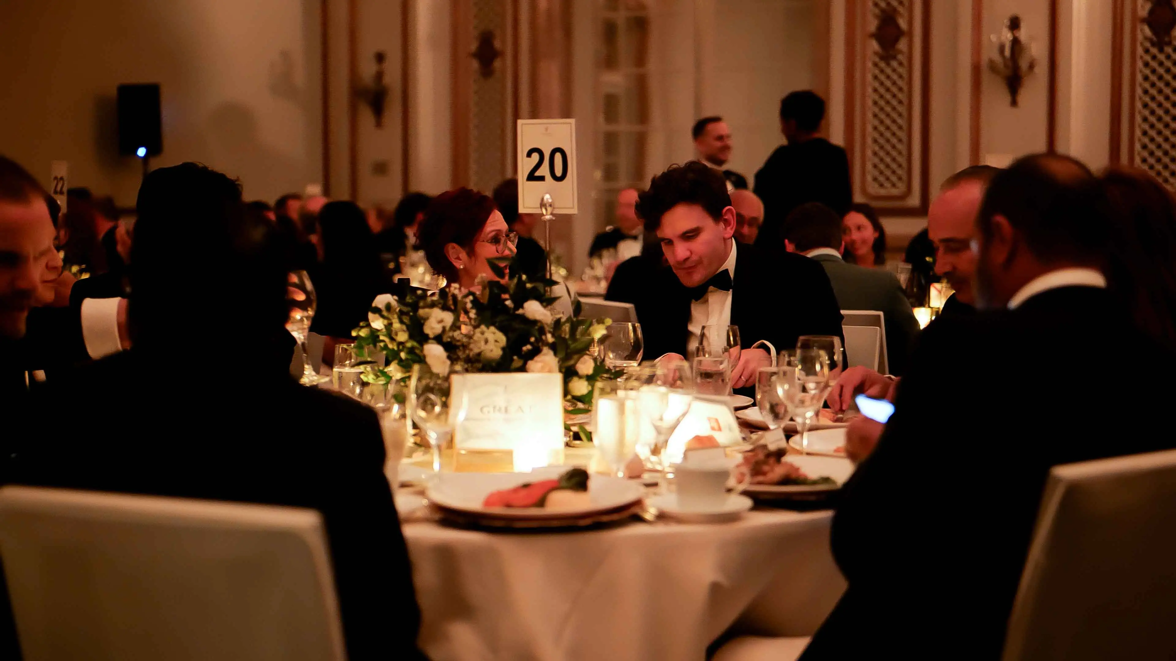 Guests dining and conversing at elegantly set tables during the GREAT GBx Gala 2024 at the Palace Hotel San Francisco, featuring floral centerpieces, candlelight, and formal attire.