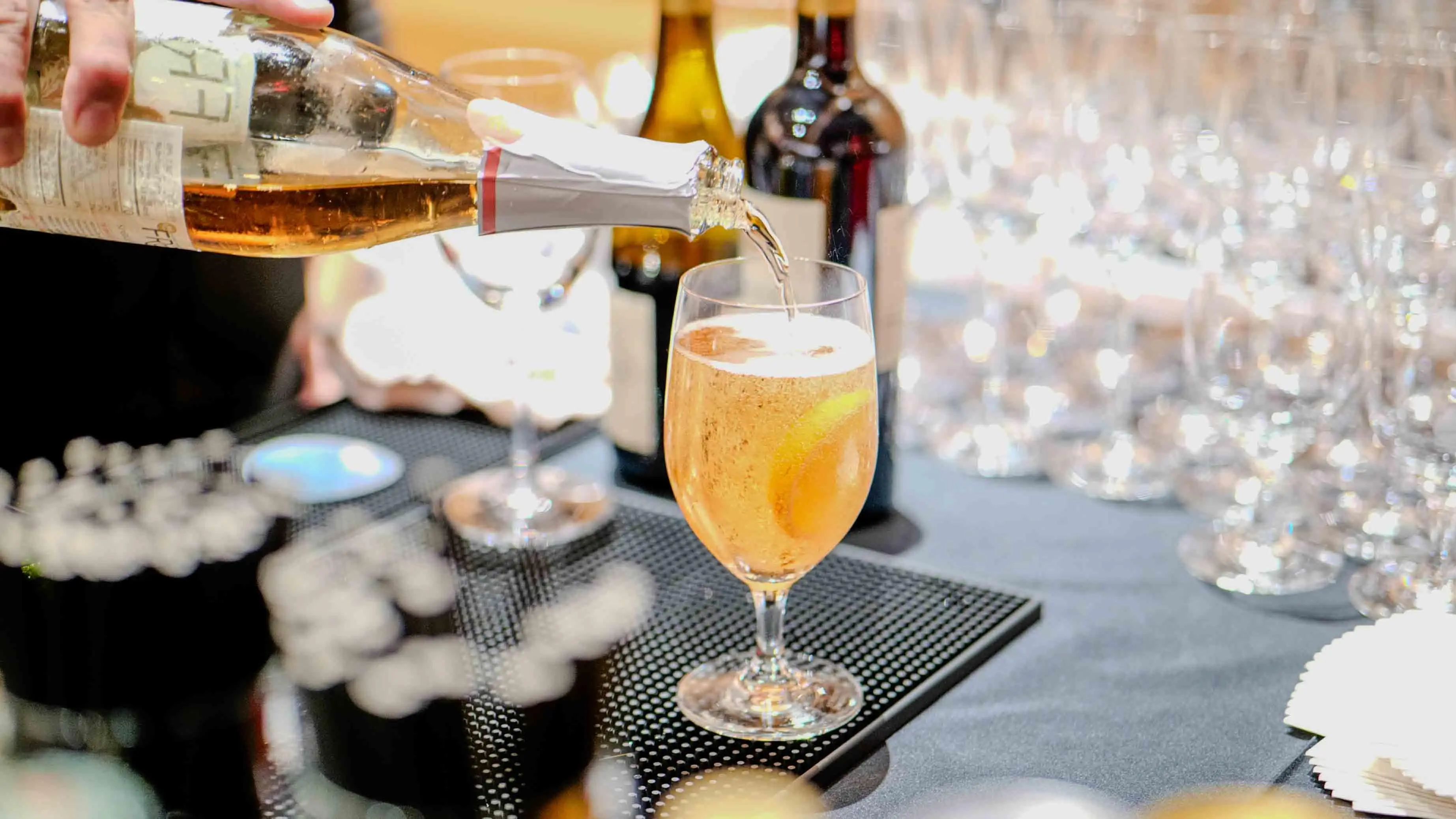Sparkling wine being poured into a glass with a citrus garnish at the bar during the Virgin Atlantic and British Consulate celebration event in San Francisco.