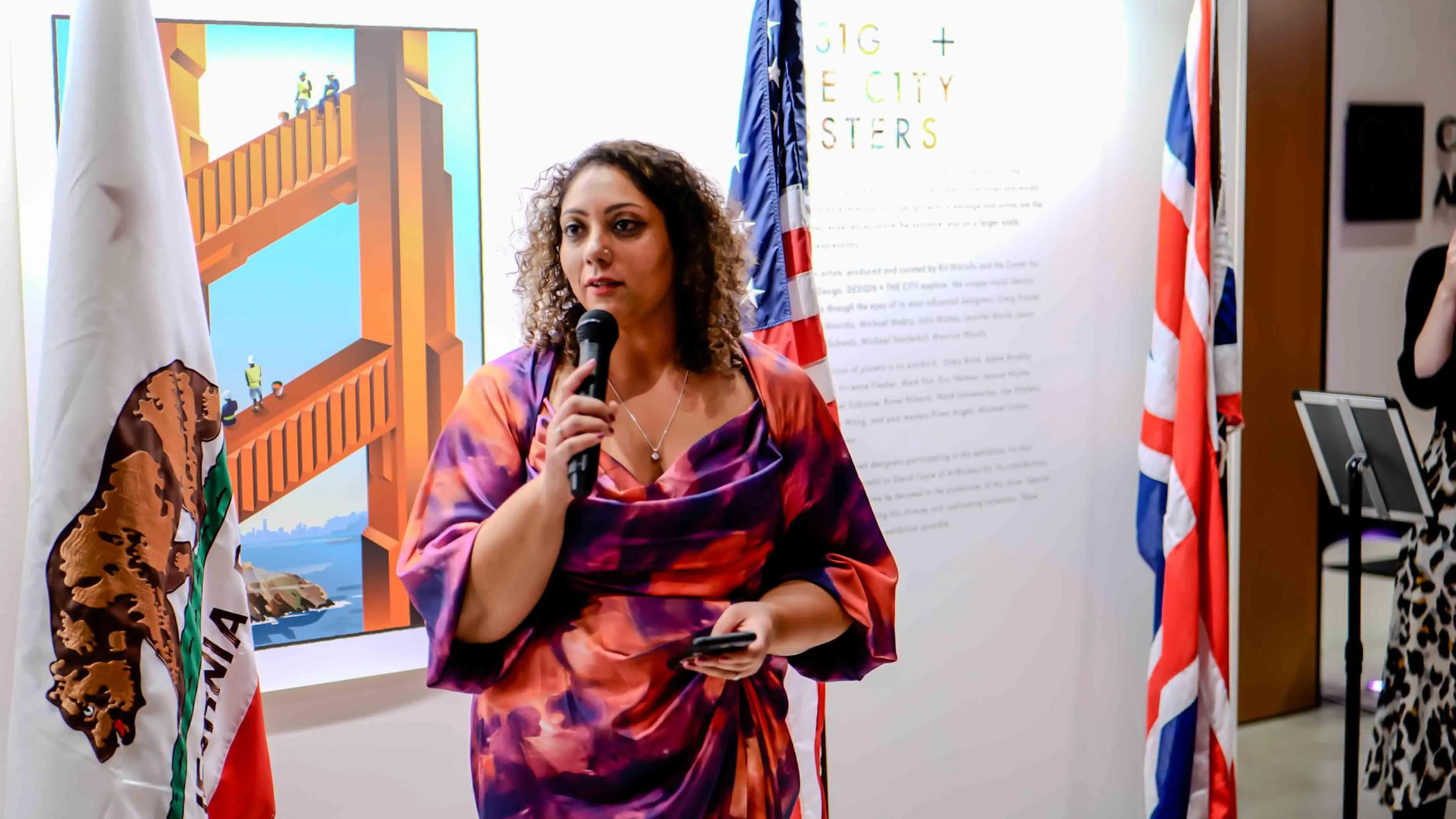 Tammy Sandhu, British Consul General in San Francisco, delivering opening remarks during the Virgin Atlantic 30-year celebration event at the Center for Architecture + Design, with U.S., UK, and California flags in the background.