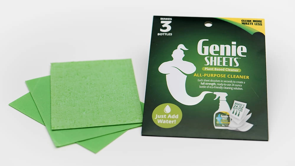 Studio product photo of Genie’s Sheets all-purpose cleaner packaging beside green cleaning sheets on a white background.