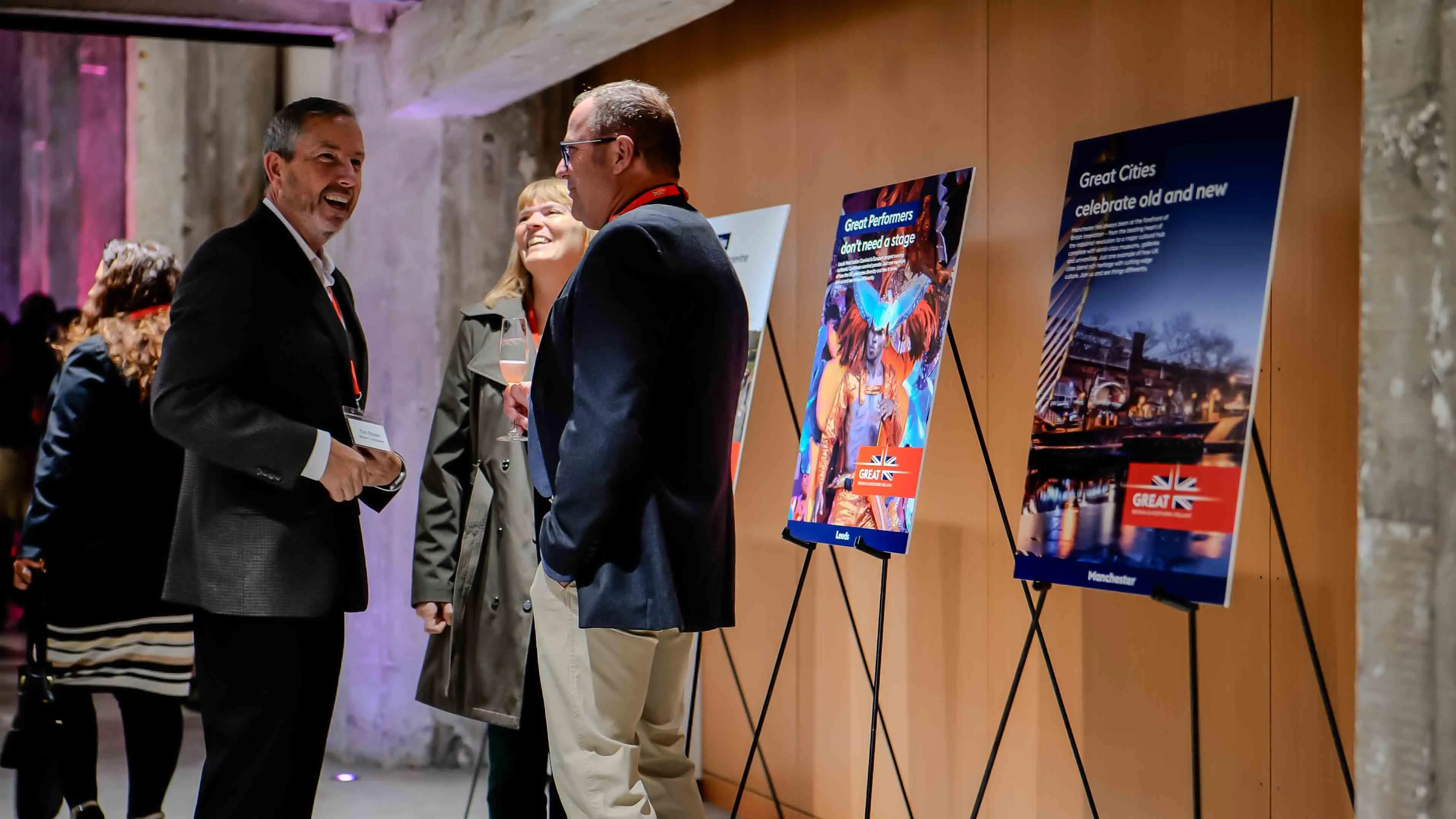Attendees conversing near UK tourism posters during the Virgin Atlantic and British Consulate 30-year celebration event at the Center for Architecture + Design in San Francisco.