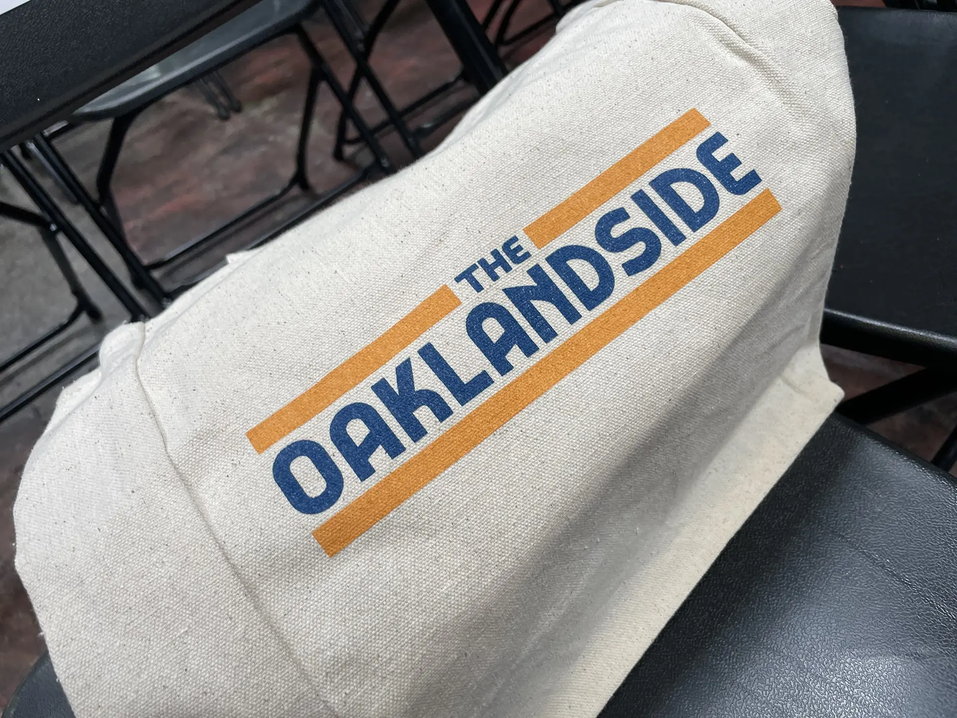 Close-up of a canvas tote bag featuring “The Oaklandside” logo, placed on a chair at the Black Political Power Tour – Oakland event hosted at Oakstop.