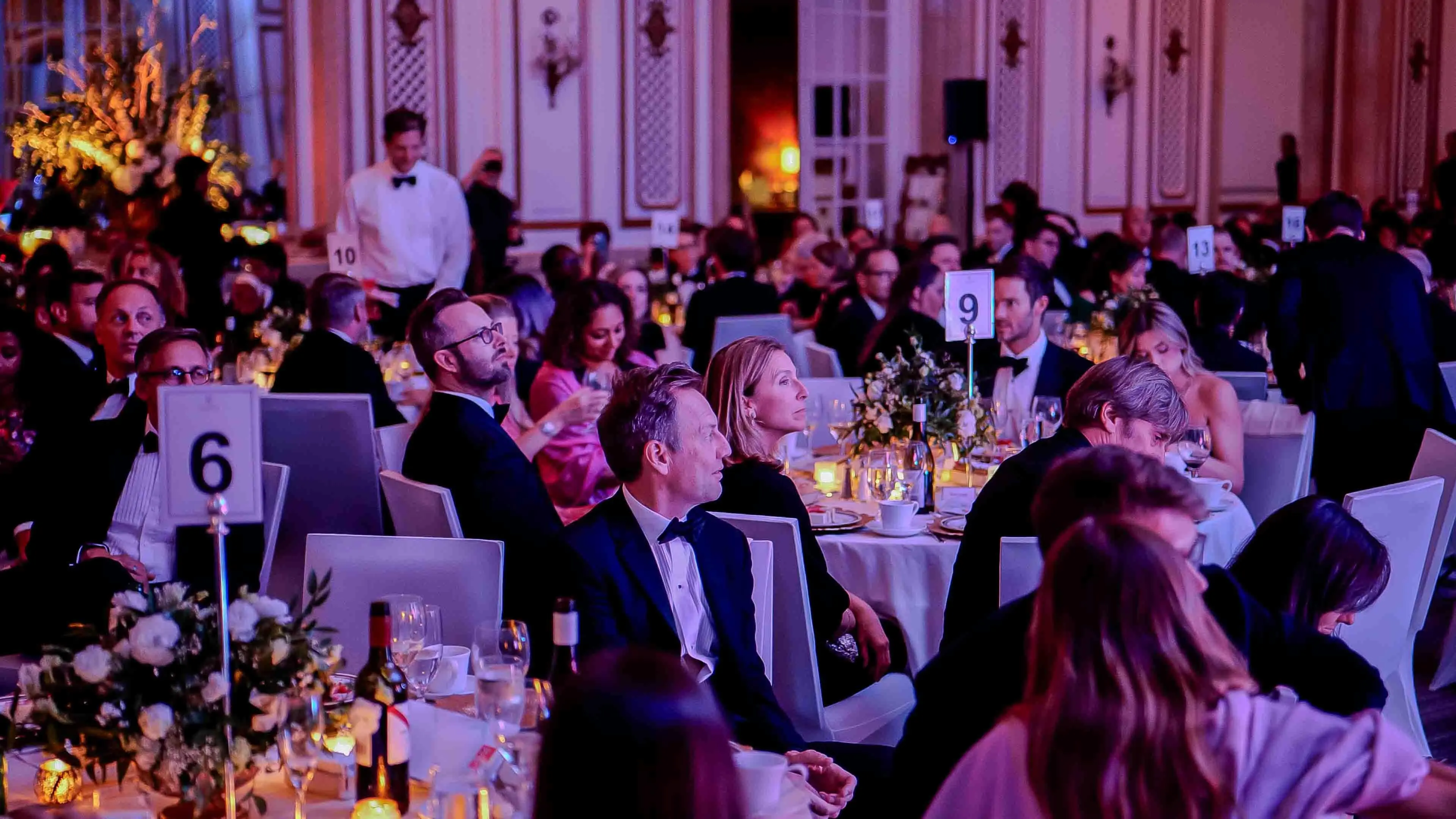 Guests seated at banquet tables attentively watching the stage during the GREAT GBx Gala 2024 at the Palace Hotel in San Francisco, surrounded by candlelight and elegant floral arrangements.
