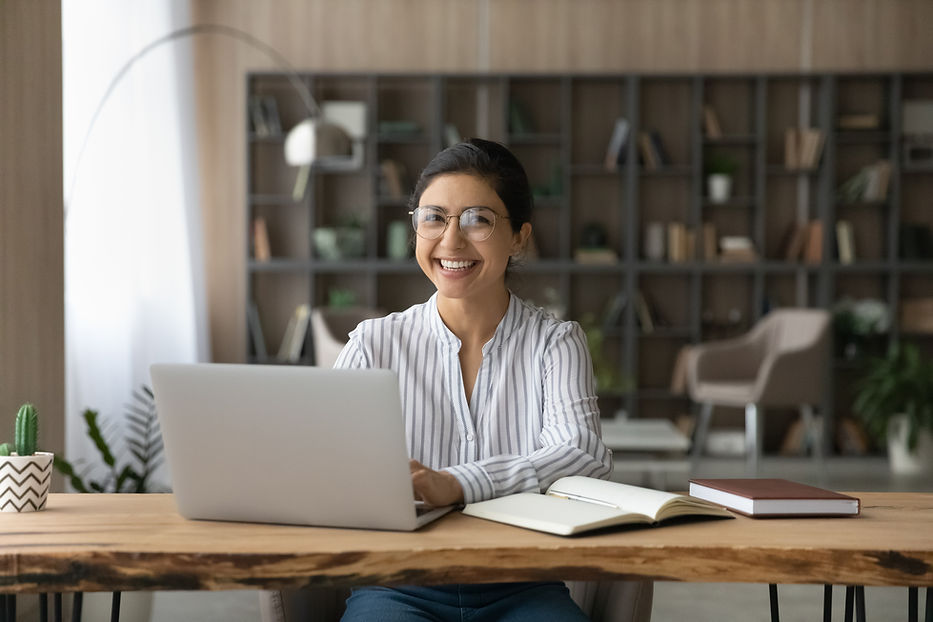 Portrait of smiling millennial Indian female student sit at desk at home study online on l