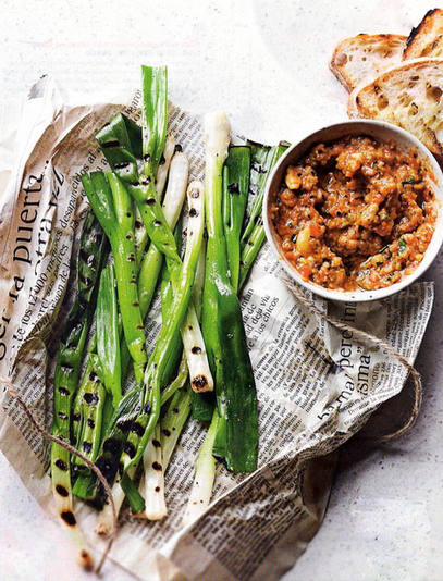 Grilled spring onions on a layer of Japanese newspaper, next to a bowl of smoked aubergine dip and a pile of crusty sourdough bread 