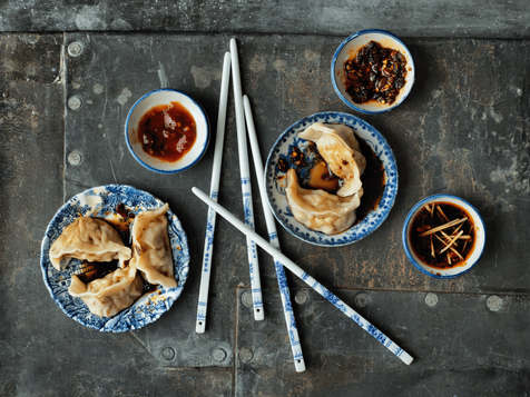 two small plates of boiled pork dumplings, served alongside chilli oil 