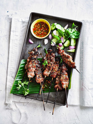 thai barbeque pork skewers with chilli sauce and chopped cucumber on a wooden tray 