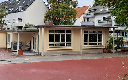Die Fassade der Kinderwelt mit großen Fenstern, davor der Außenspielbereich.