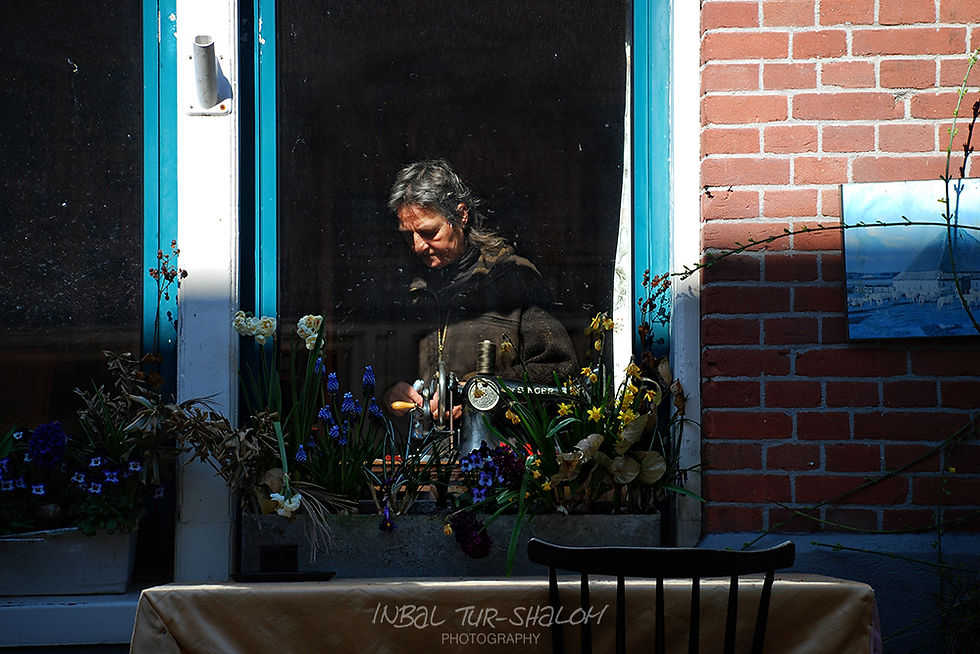 A woman stands at the window, her face lit by the sun, outside the window a planter with colorful spring flowers