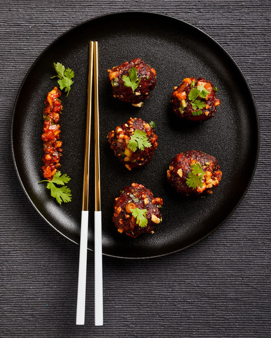 Vegetarian kulchara balls are places beautifully on a black ceramic plate. A pair of golden chopsticks rests on the plate. Artfully styled elements accompany the kulchara.