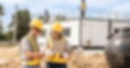 Two construction workers in yellow helmets and vests review plans on a tablet at a jobsite, supported by AI field service automation for real-time dispatch and work order updates.