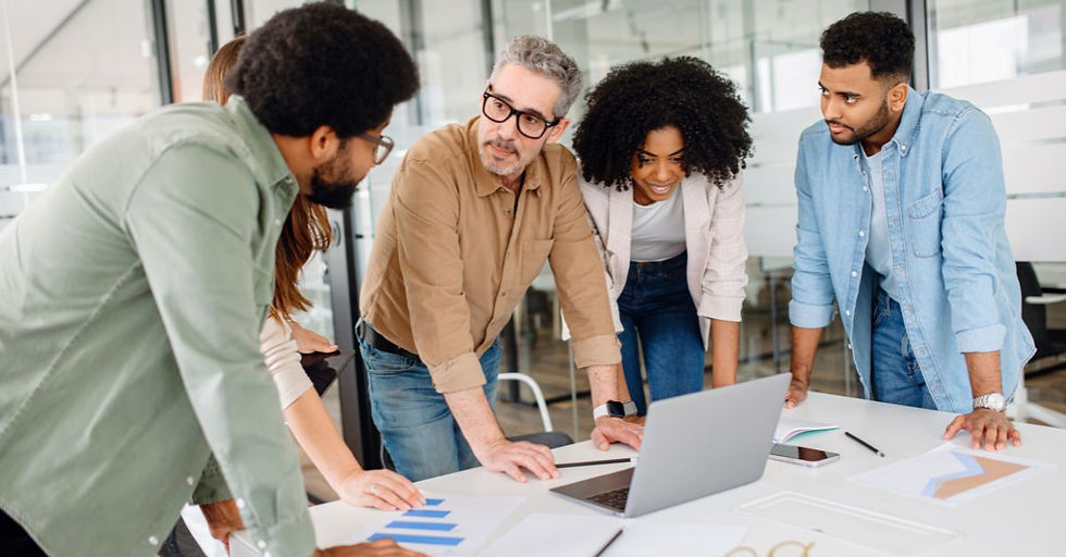 Group of diverse colleagues leaning over a table in a bright office, discussing why ERP projects fail on a laptop, with chart papers visible.