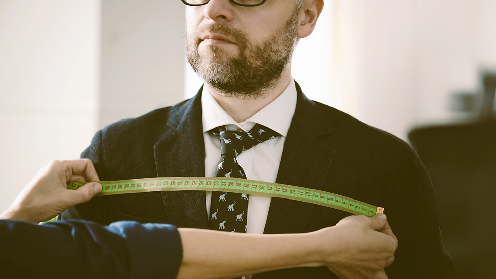 Man in a suit with a dinosaur-patterned tie is being measured with a green tape measure. Neutral background, professional setting.