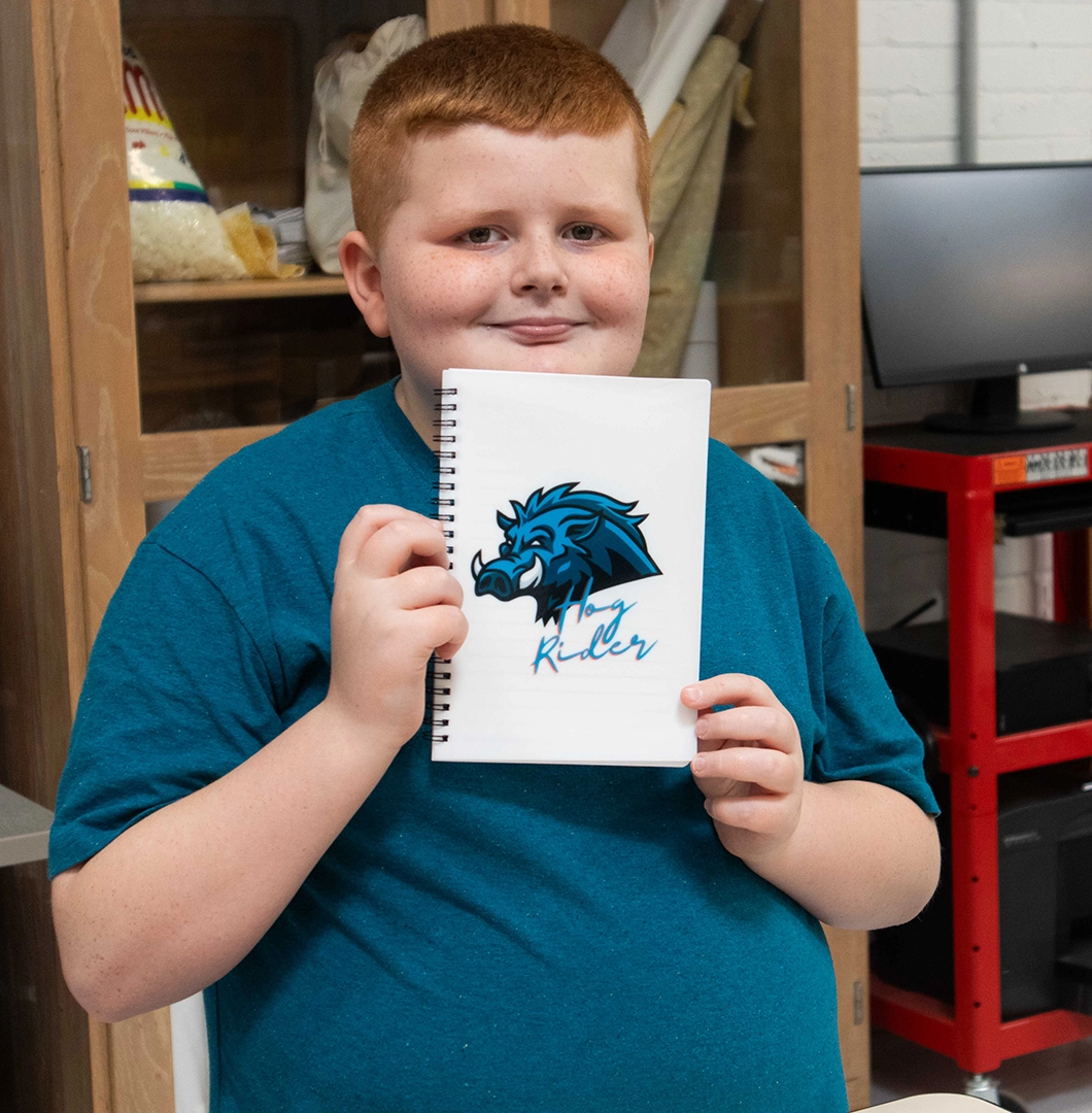 A student displays a personalized notebook cover made on the heat press