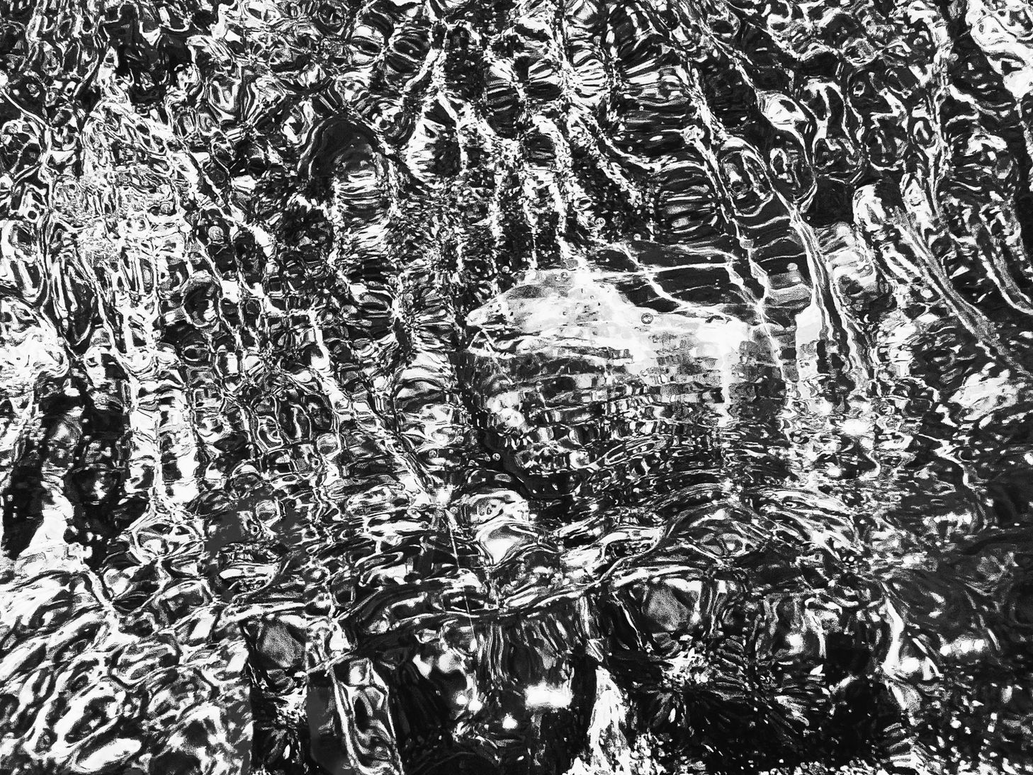 Black-and-white macrophotograph of rippling water surrounding a translucent crystalline form, with layered reflections and refracted light patterns.