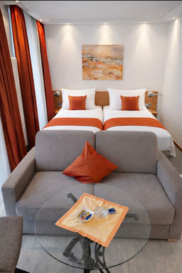 Modernes Hotelzimmer mit zwei Einzelbetten und grauem Sofa.
