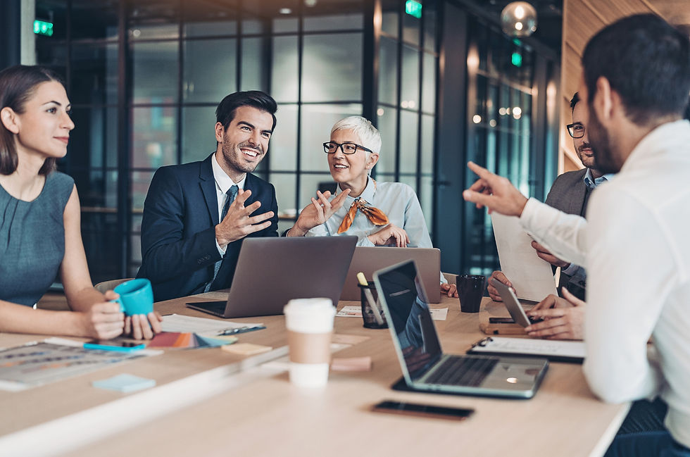 A group of professionals in a modern office, engaging in a lively discussion around a table with laptops and papers. Warm lighting sets a collaborative mood.