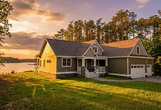 Front view of beige single-story house with gable roof, two-car garage, driveway, and trees around lawn area.