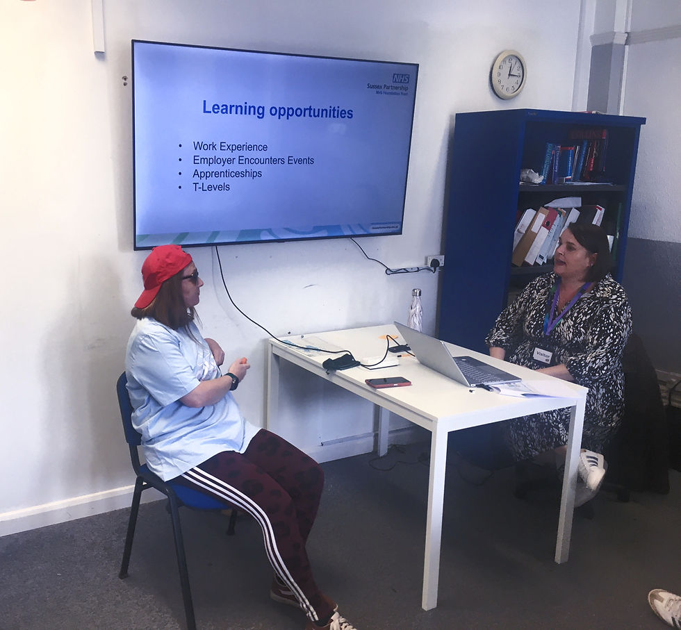 Two people talk in an office. The screen displays "Learning opportunities." One wears a red cap, the other sits by a laptop. Clock on the wall.