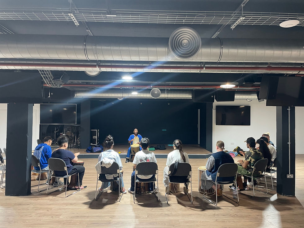 young people sat in a semi-circle each with an African drum facing an instructor