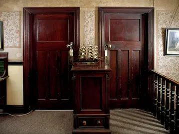 two brown wooden doors in a wall with model ship on a stand between them