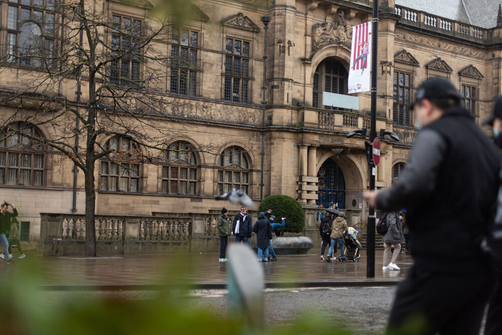 A photo of people walking past an old-fashioned big Victorian building on a rainy day