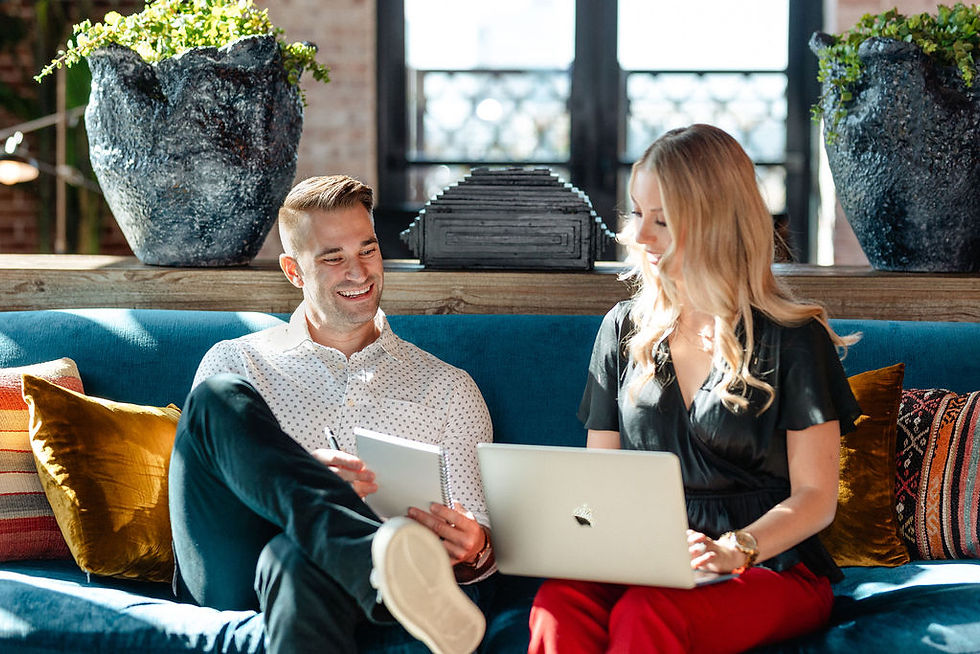Man with notebook and woman with laptop smiling and talking on a teal couch
