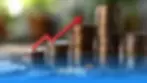 Stacks of coins with a red arrow on them in front of a blurry background and red