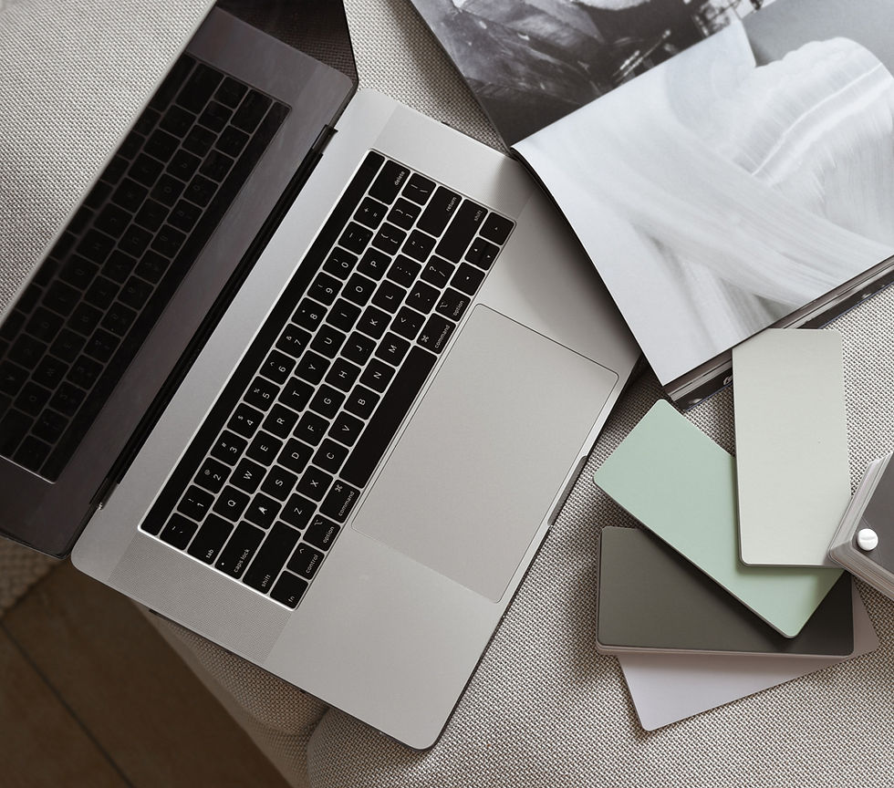 Open laptop on a neutral-toned fabric surface with a design book and paint swatches in shades of green, gray, and white, suggesting interior design inspiration.