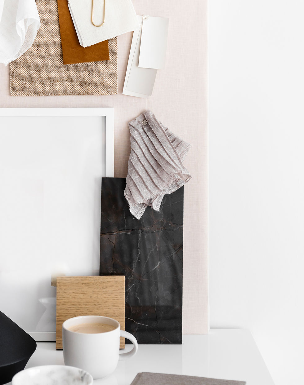 Interior design mood board with fabric swatches, paint samples, wood and stone materials, and a cup of coffee on a white desk.